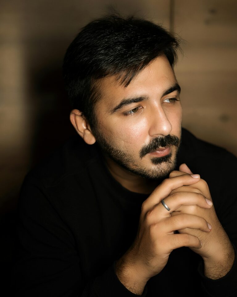 A thoughtful man with facial hair, hands clasped, wearing a ring, captured indoors.